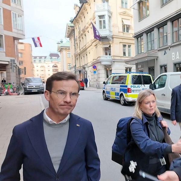 Personer promenerar på gata med polisbilar och en Infrago-skåpbil i bakgrunden.