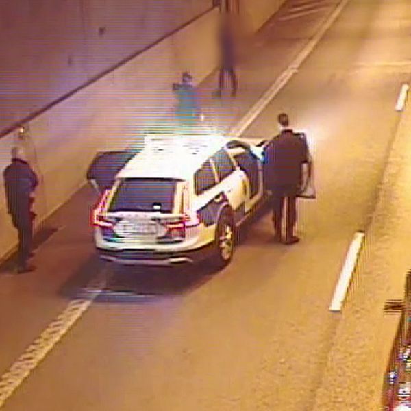 En polisbil med flera poliser närmar sig en man till fots i en biltunnel.