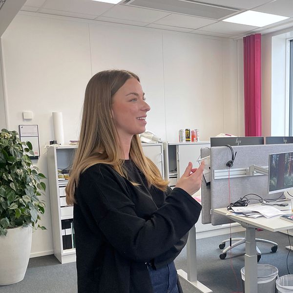 Två personer samtalar i ett kontorslandskap med stora fönster och arbetsplatser i bakgrunden.