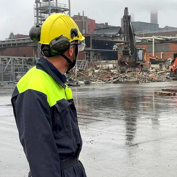 Två personer i skyddskläder blickar ut över ruinerna vid Rönnskärsverken