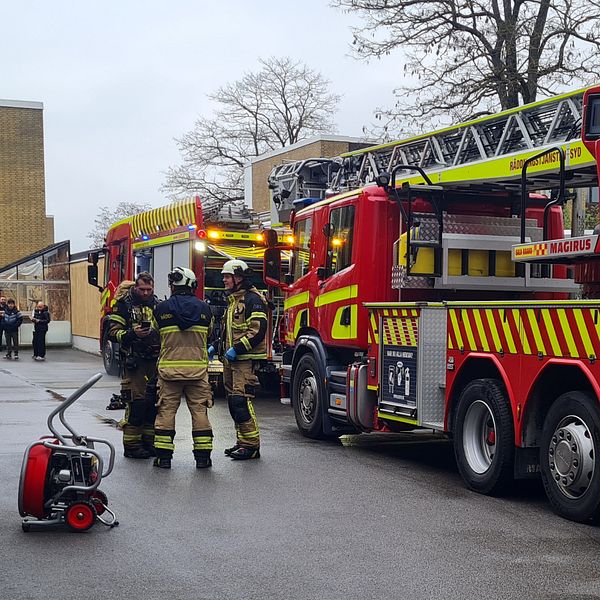 Brandbil med uppfälld stege och brandmän på väg vid höghusområde.