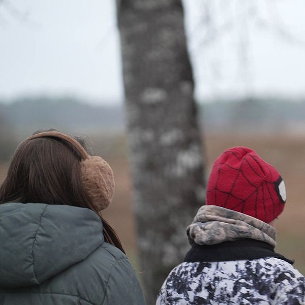 Tre barn står med ryggen mot kameran och tittar ut över ett landskap.