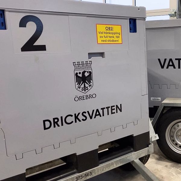 Två stora behållare märkt ”Dricksvatten” och ”Vatten” från Örebro, placerade på släpvagnar inuti en byggnad. En gul skylt varnar för att behållarna endast får hanteras med godkänd utbildning.