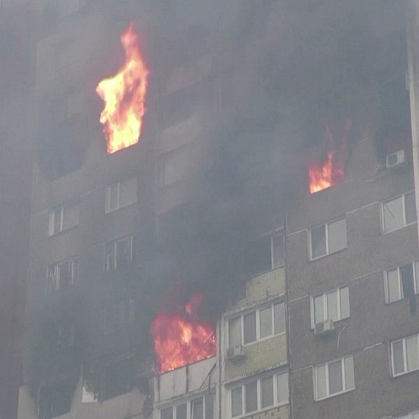 Ett lägenhetshus brinner och en kvinna med en luva uppdragen