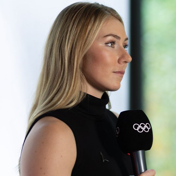 En delad bild som visar två personer i professionella sammanhang. Till vänster en kvinna som håller i en mikrofon med Olympiska ringarna, klädd i svart. Till höger en man i en blå jacka med FIS-logotyp som talar i en mikrofon.
