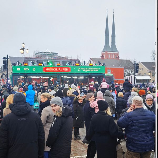 Stortorget i Växjö på ena sidan där Musikhjälpen-glasburen och människor syns stå på torget. På andra sidan en bild på en ung kvinna i brun mössa och röd jacka, som svarar på frågor i en SVT-mikrofon
