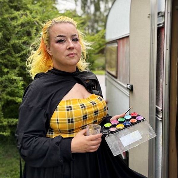 Angiie Dahlö står utanför en husvagn och håller i färgpalett och pensel.