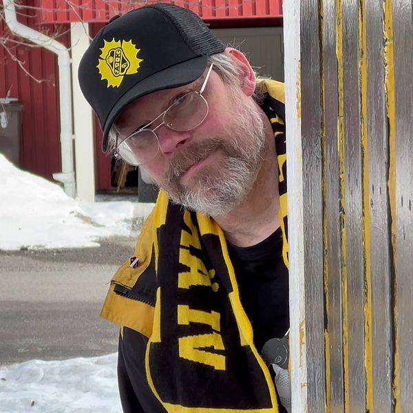 Hockeyfan med Skellefteå AIK-keps tittar fram bakom husvägg.