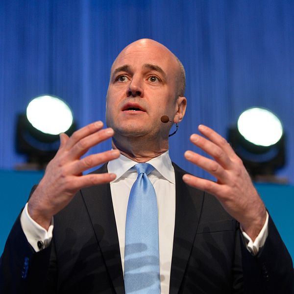 Till vänster fredrik Reinfeldt som gestikulerar med båda händerna och bär en mörk kostym med ljusblå slips. Till höger Ulf Kristersson som har på sig en mörk kavaj över en ljus skjorta.