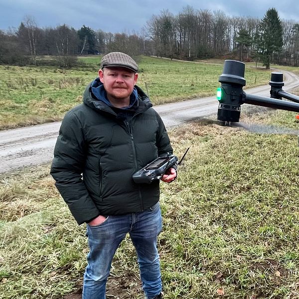 Mattias Pettersson står på ett fält med en drönare svävande framför sig i luften.