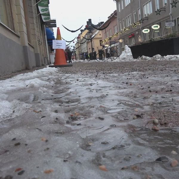 En delad bild som visar två sektioner: till vänster syns en isig och snöig gata i en stad med butiker och dekorationer, medan det till höger visas en man i vit arbetskläder med namnskylt som anger hans yrke som läkare.