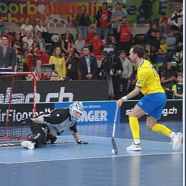 En delad bild som visar två scener. I den vänstra sektionen ses en innebandymatch där en svensk spelare skjuter mot mål, medan målvakten i svart knäböjer för att blockera bollen. Den högra sektionen visar SVT:s reporter Kamil Bochenski som står framför en grå bakgrund och använder händerna för att illustrera något.