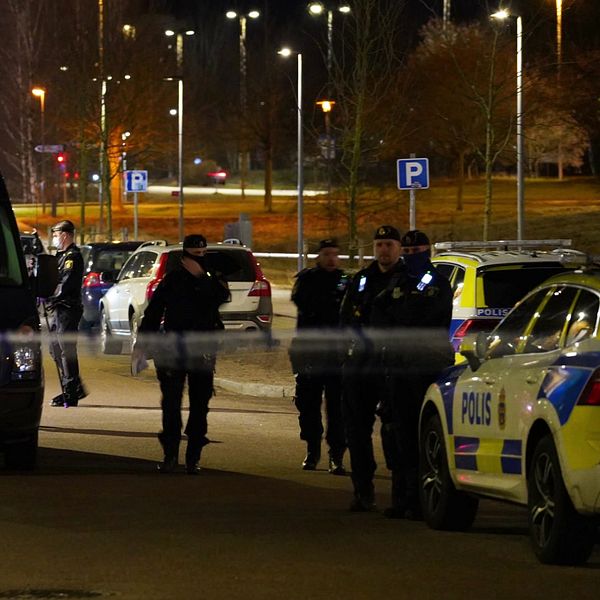 Poliser i uniform står vid flera polisfordon på en parkeringsplats under natten, med gatubelysning i bakgrunden. Till höger syns en person som rapporterar, iklädd en varm jacka och en stor halsduk, som håller i en mikrofon med SVT:s logotyp.