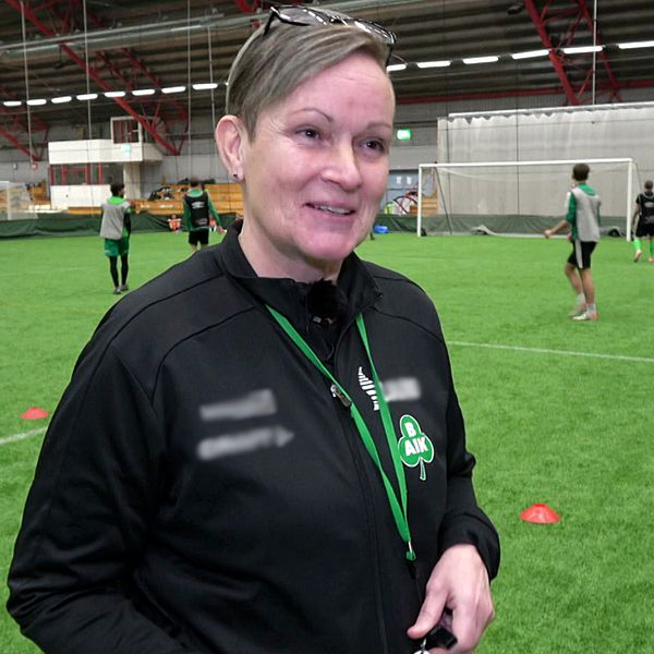 Fotbollstränaren Carola Karlsson med visselpipan i hand och en fotbollsspelare i Bergnäsets AIK i klädd grön tröja och orange väst.