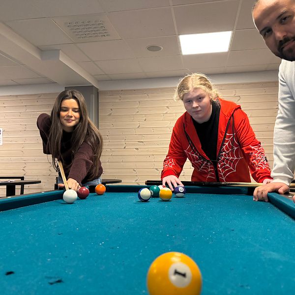 Amela Softic, Emma Mitchell och Ali Muhson spelar biljard; mobilskåp syns till höger.