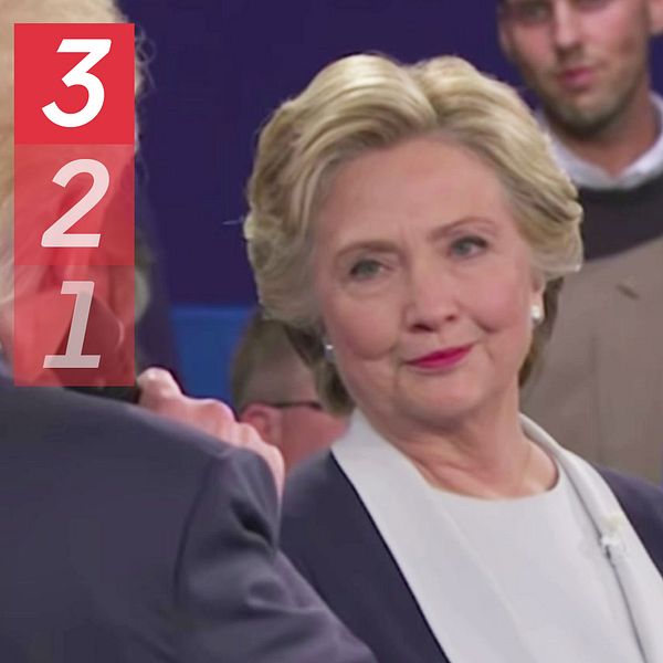 En scen från en debatt där Donald Trump talar till Hilary Clinton. I bakgrunden syns flera personer som observerar händelsen. Till höger en bild på George W. Bush.