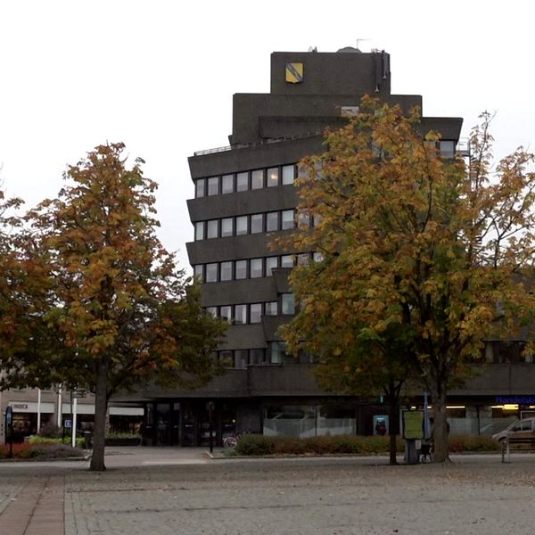 En delad bild som visar två sektioner. Den vänstra sidan visar Vetlanda kommunhus, en modern, fler våningar hög byggnad med träd i förgrunden. Höger sida Georg Grönwald, kommunikation- och utvecklingschef Vetlanda kommun. Visar en man i en mörk kappa som står framför en rödbrun tegelbyggnad.