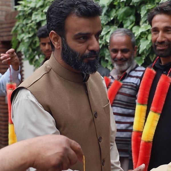 Lokalpolitiker i Kashmir. Man med väst och skägg. Fotgängare i Kashmir, berg i bakgrunden.