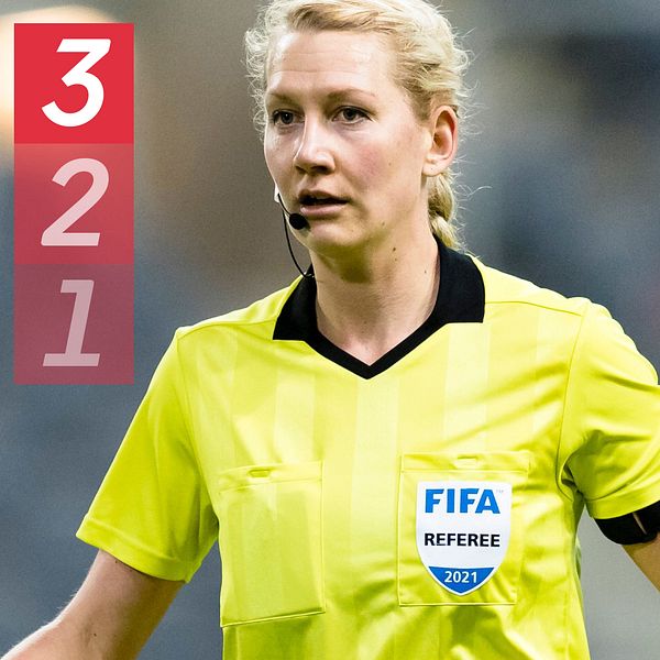 Kvinnlig fotbollsdomare i gul tröja och FIFA-emblem på bröstet.