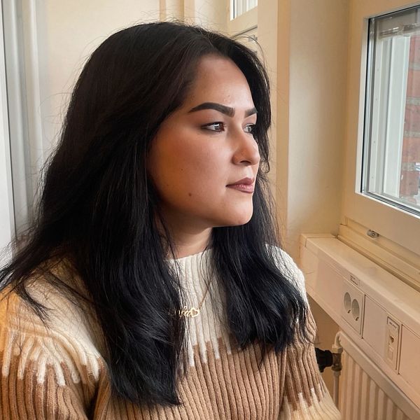 En kvinna med långt mörkt hår som tittar ut genom ett fönster