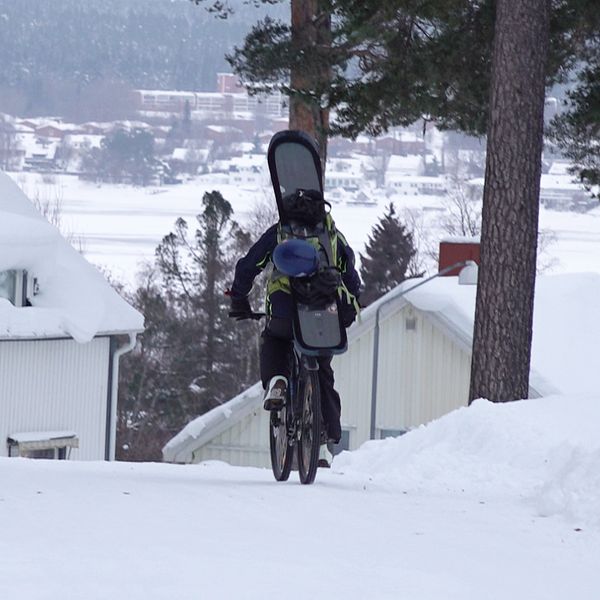 En kille cyklar med en snowboard på ryggen i närheten av Gustavsbergsbacken på Frösön i Östersund.