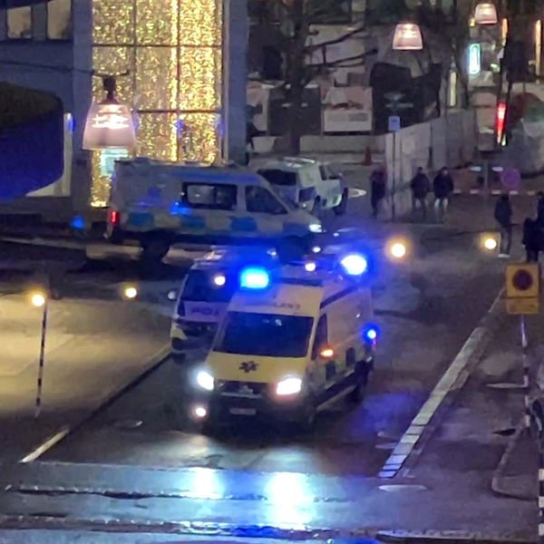 En delad bild som visar två scener relaterade till en nödsituation. Den vänstra sektionen visar en gata belyst av blåljus från en ambulans och en polisbil med människor som rör sig i bakgrunden. Den högra sektionen visar en hand som håller i en pistol i svartvitt, vilket skapar en dramatisk kontrast till scenen till vänster.