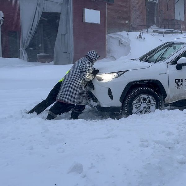 Två personer försöker få loss en bil från en snöhög.