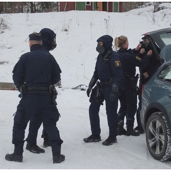 Maskerade poliser med skyddsutrusning vid en bil, polis som blir intervjuad.