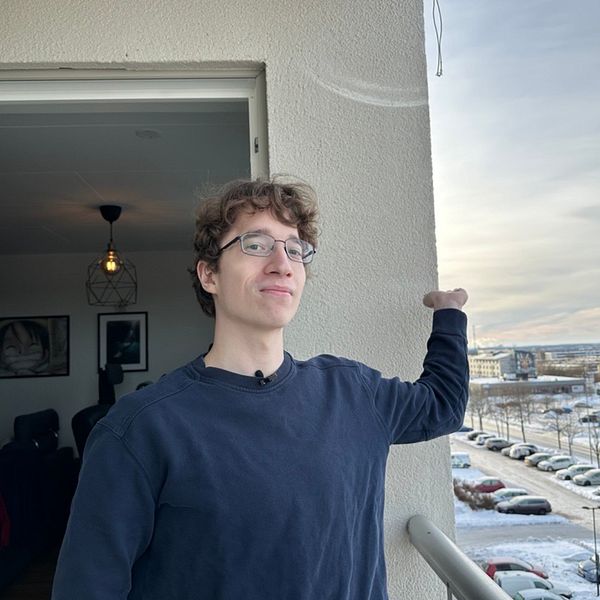 En person står på en balkong och pekar mot en panoramautsikt med snö och parkerade bilar i bakgrunden, till vänster. Till höger finns en närbild av en säkerhetskamera som är monterad på väggen, riktad mot samma utsikt.