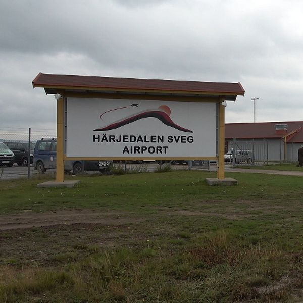 Mathias Wigren vid Härjedalen Airport och flygplatsens skylt utomhus.