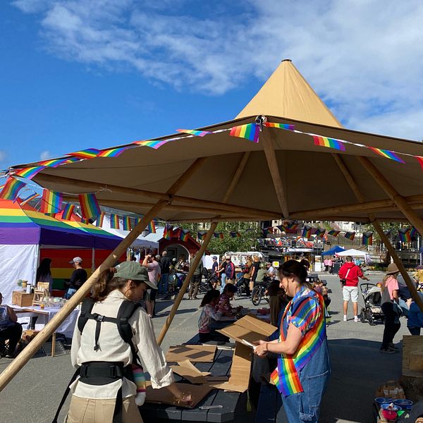 Delad bild. Till vänster: Pridefestivalen, Åre torg som under festivalen kallas regnbågstorget. Mycket prideflaggor och tält med utställare. Till höger: Besökaren Johannes Jakobsson i vit t-shirt.
