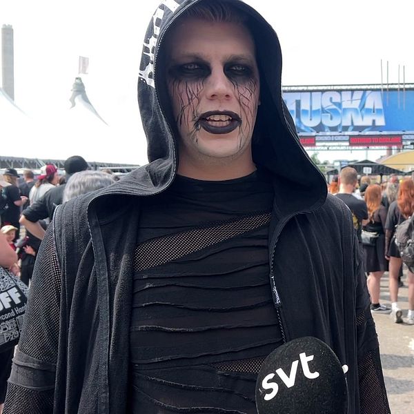 Tuska-festivaalivieras mustassa asussa metallifestareilla, taustalla festivaalikävijöitä