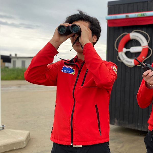 Ungdomar som hjälper räddningstjänsten tittar i en kikare på stranden.