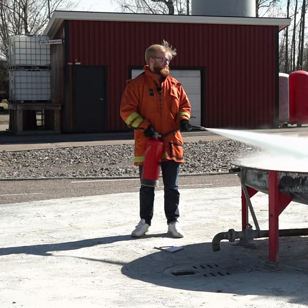 En man iförd skyddskläder sprutar med en brandsläckare på en eld vid räddningstjänstens testplats i Karlstad.