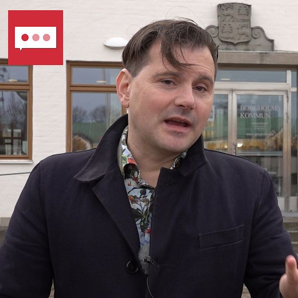 Personen, Joel Schäfer (S), ordförande i socialnämnden i Borgholms kommun gestikulerar och talar framför en byggnad med en dörr som visar namnet Borgholms kommun. I bakgrunden syns en orange pumpa och fönster med synligt ljus. Det är en grå och mulen dag.
