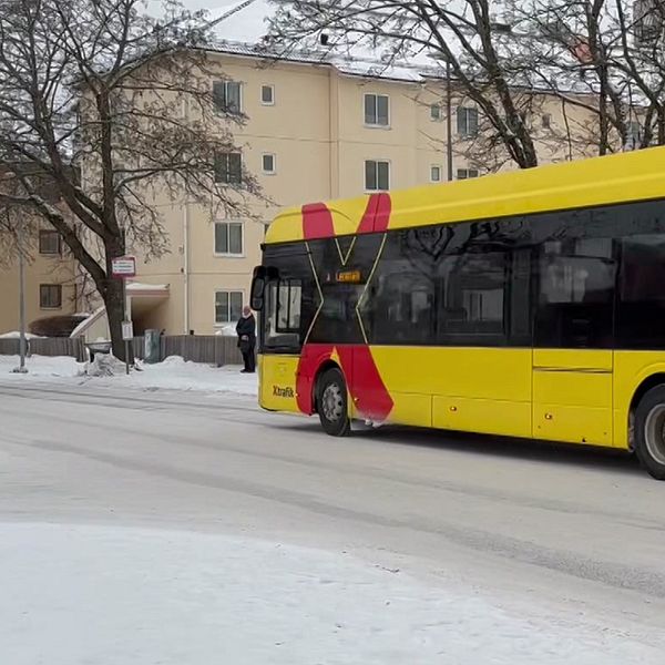 En buss som är röd och gul med ett stort X på sidan kör på en vinterväg.