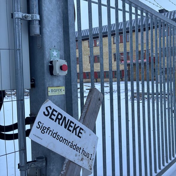 Stängd metallgrind i ett snöigt område, med en skylt som visar ”SERNEKE” och ”Sigfridsområdet hus 1”.