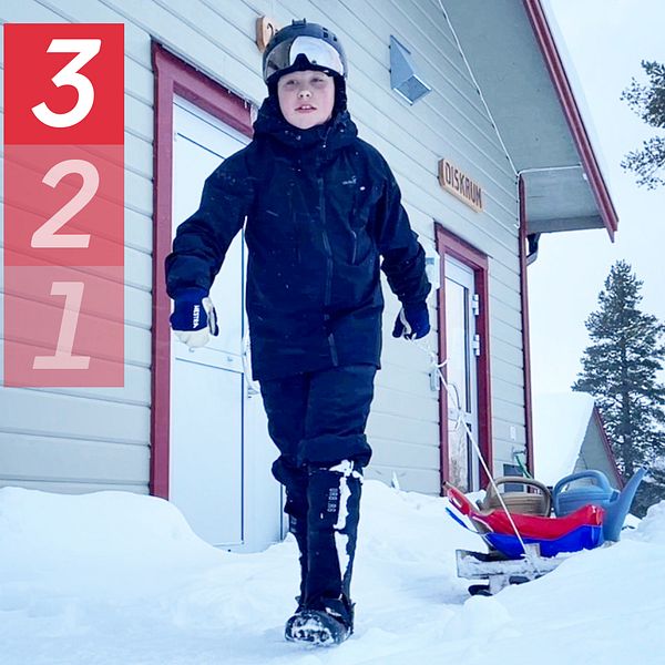 Ett barn med svart hjälm drar en egenbyggd pulka med vattenkannor på bakom sig i snön.