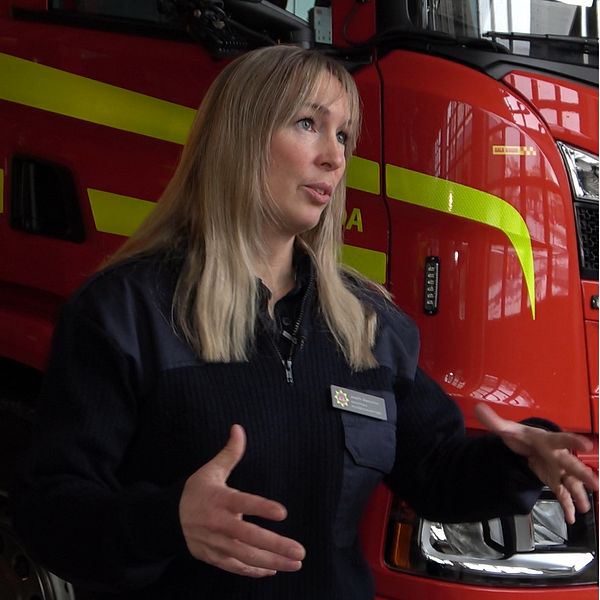 Kvinna framför brandbil, hus som brinner