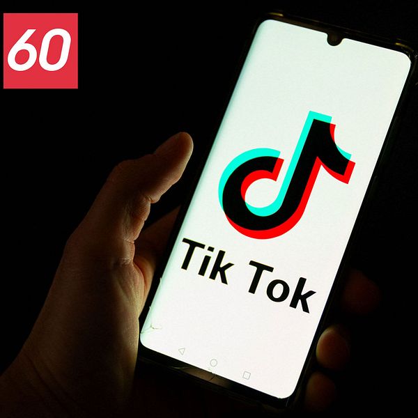 En hand som håller en mobiltelefon i mörkret där det står ”Tiktok” på mobilskärmen. En Tiktoklogga syns på skärmen.