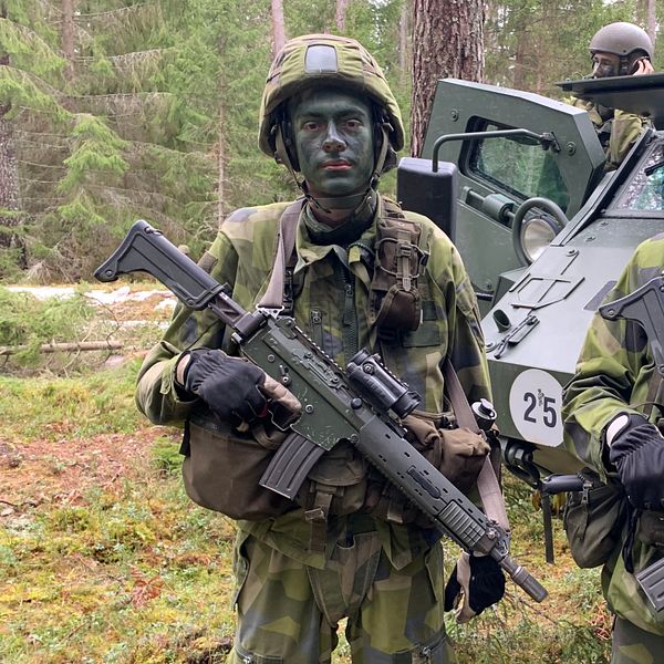 Värnpliktiga män med vapen tittar in i kameran