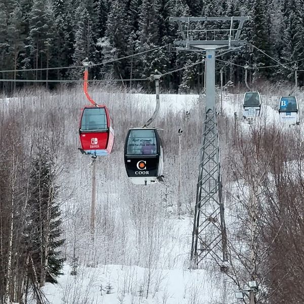 En delad bild visar en skidbacke med en rad av skidliftgondoler som löper genom ett snötäckt landskap. Vid sidan av denna scen finns en suddig bild av en person som håller en mikrofon med SVT-logotypen.
