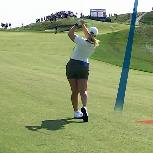 Kvinnlig golfspelare slår ut på banan och ler med klubba i handen.
