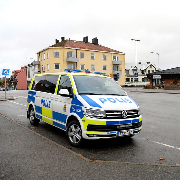 En polisbil står parkerad på en tom gata i en stadsmiljö med bostadshus och en mindre byggnad i bakgrunden under en molnig himmel.