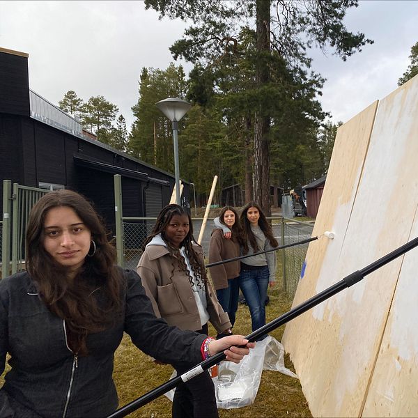Fyra personer målar en stor vägg utomhus med hjälp av färgrollers.
