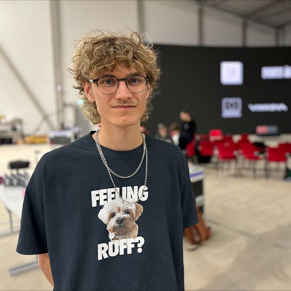 Person i t-shirt med hundtryck i väst, bakom en stolsrad och stor svart scen.
