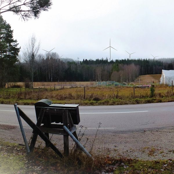 En landsväg i förgrunden med vindkraftsnurror i horisonten