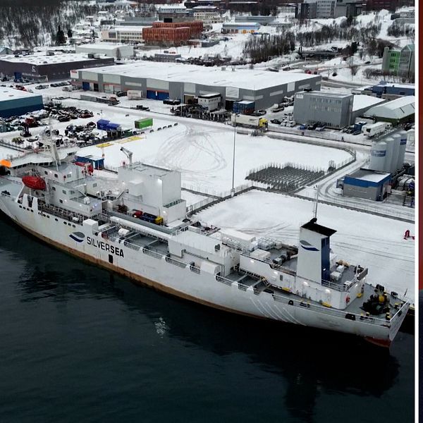 Deltad bild: Till vänster syns ett stort fartyg vid en snötäckt hamn med flera byggnader och lastbilar i bakgrunden.