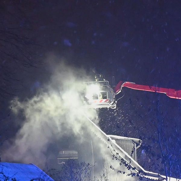 Rök stiger från ett villatak och räddningstjänsten släcker från kran.