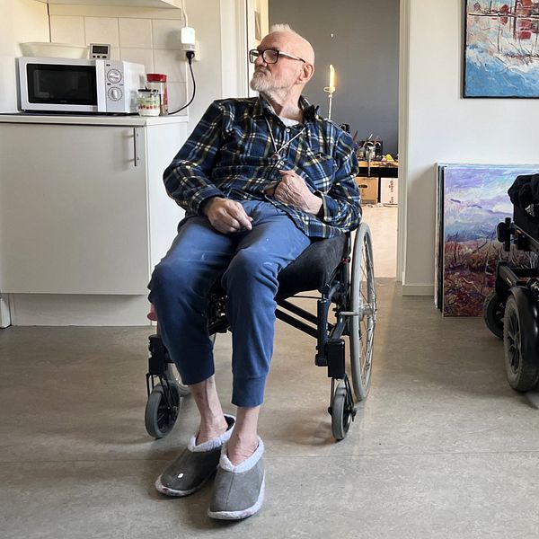 Äldre man i rullstol tittar fundersamt åt sidan i sitt kök.